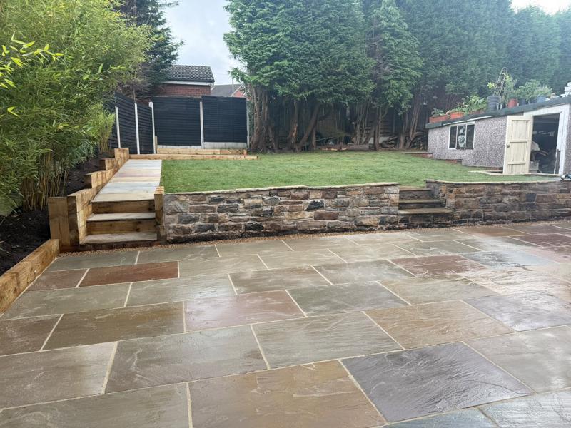 Sandstone patio with a dry stone retaining wall, sleeper beds and steps to a lawn
