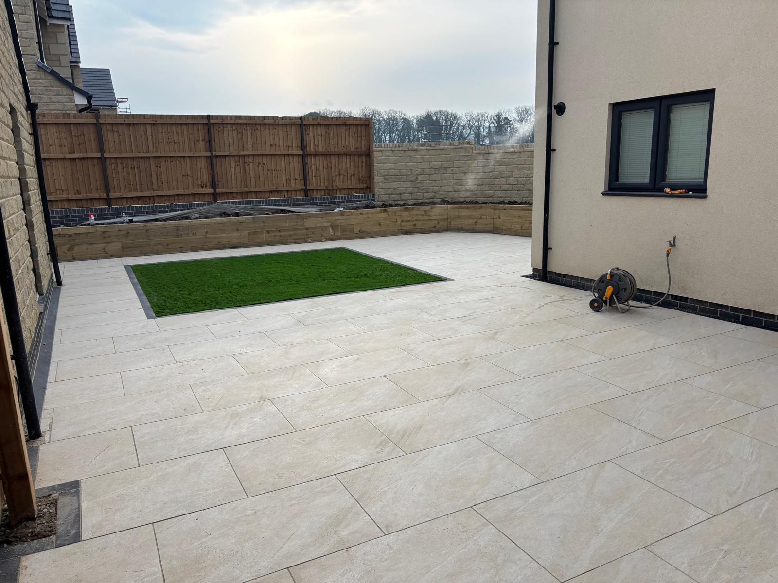 Pale porcelain patio wrapping around a new build house with an inset lawn